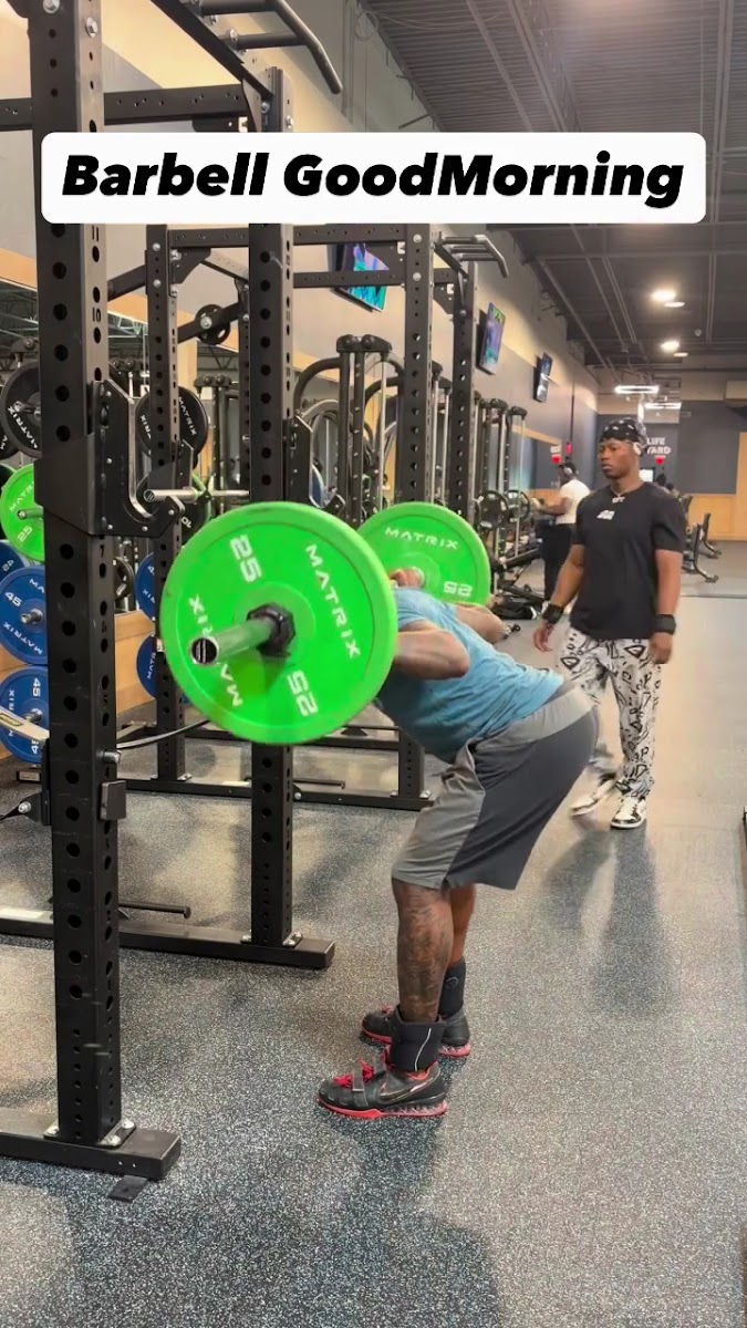 Coach spotting a client through a barbell good morning with green bumper plates
